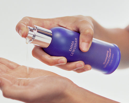 Hand holding a purple bottle of Emma Lashwam skincare product against a white background